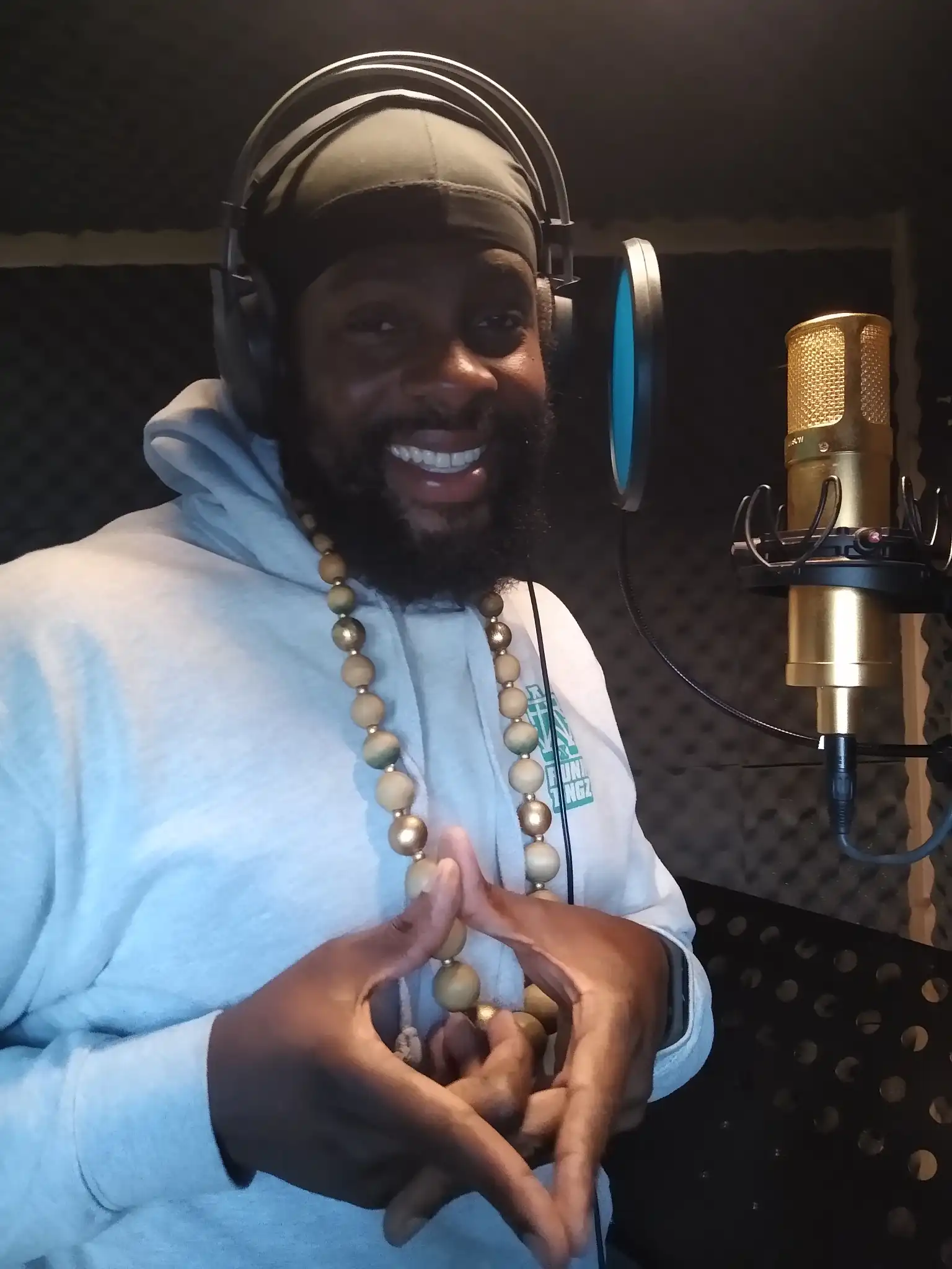 a man wearing headphones and wearing a beaded necklace in front of a microphone